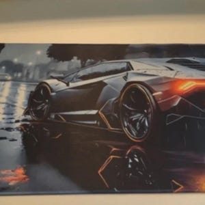 May include: A black and gray mousepad featuring a sleek, modern sports car design. The car is depicted in a rainy environment with orange taillights and reflections on the wet surface. The overall theme is automotive.