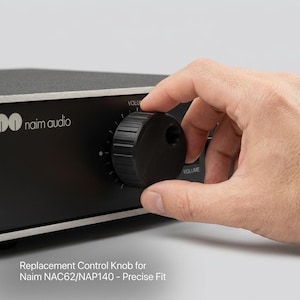 May include: A black replacement control knob for Naim NAC62 and NAP140 audio equipment. The cylindrical knob features a textured, ribbed edge for grip and a circular indentation on its face. It is mounted on a black audio device panel.