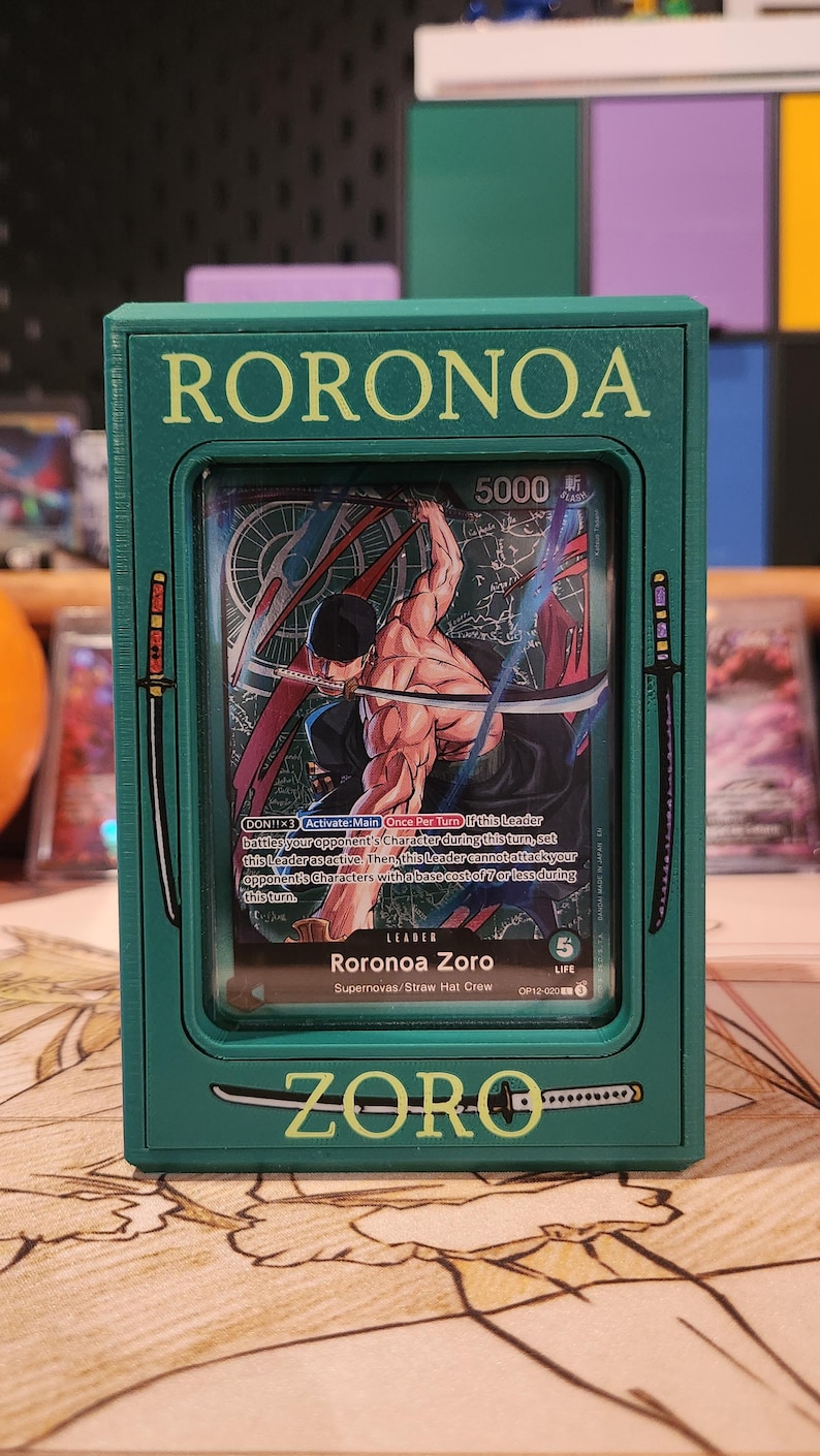 May include: A green card holder featuring a card with the name "RORONOA" at the top. The card inside depicts a muscular character with swords. The text "ZORO" is at the bottom.