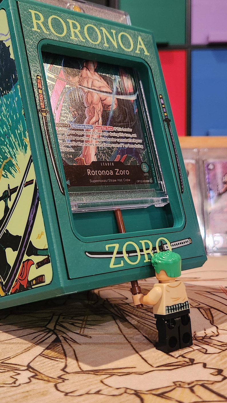 May include: A green card holder with the name "RORONOA" at the top and "ZORO" at the bottom. Inside the holder is a card featuring a character named Roronoa Zoro. A small Lego figure of Zoro is holding a sword. The card holder has a sword design.