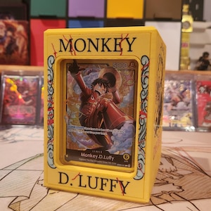 Op de afbeelding: Een gele kaarthouder met de zwarte tekst "MONKEY" en "D.LUFFY". De houder toont een kaart met een personage in een rode outfit. De kaart heeft de tekst "Monkey.D.Luffy" en "5000".