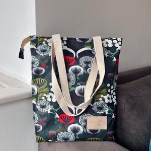 Op de afbeelding: Een tote bag met een donkergroen bloemenpatroon met witte, rode en groene accenten. De tas heeft crèmekleurige handvatten en een leren label met de tekst "MATERIA LAB". De tas is gemaakt van een duurzame stof.