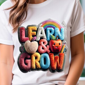 Peut inclure: T-shirt blanc avec un motif coloré affichant les mots "LEARN & GROW". Le design comprend un arc-en-ciel, une pomme souriante, un crayon et des motifs de cœur et de lettres duveteux. Le t-shirt a un col rond classique.