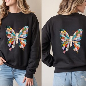 Peut inclure: Sweat-shirt noir orné d'un motif de papillon coloré en patchwork sur le devant et le dos. Le papillon est composé de tissus multicolores. Le sweat-shirt a un col rond et des manches longues. Le design est une caractéristique importante.