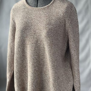 May include: A neutral-toned sweater with a textured knit design. The long-sleeved top has a round neckline and a slightly loose fit. The fabric appears to be a blend of beige and brown threads, creating a speckled effect. The sweater is displayed on a mannequin.