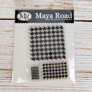 May include: Clear stamp set by Maya Road featuring a black and white houndstooth pattern. The set includes three stamps of different sizes, packaged in a clear plastic sleeve. The text "Maya Road for the journey of a lifetime" is printed on the packaging.