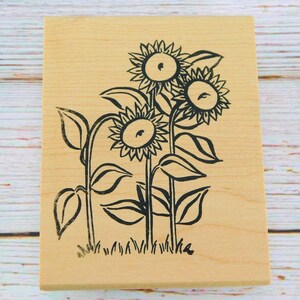May include: A wooden stamp with a black and white design of three sunflowers with stems and leaves.