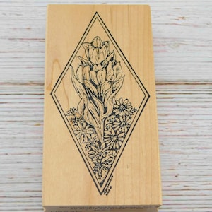 May include: A wooden stamp with a black and white illustration of a flower in a diamond shape. The flower is a cluster of tulips with smaller flowers surrounding the base.