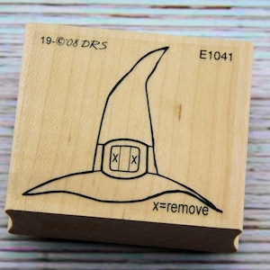 May include: Wooden rubber stamp with a black line drawing of a witch's hat. The hat has a pointed top and a wide brim. The stamp is labeled "E1041" and "x=remove".