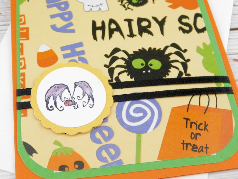 May include: Halloween-themed greeting card with a yellow background featuring a black spider, candy corn, and the words "HAIRY SC" and "Trick or treat". A circular sticker with purple bat-like creatures is also present.