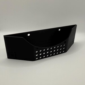 May include: A black, wall-mounted storage basket with a rectangular shape and a series of small, evenly spaced holes along the front. The basket has a slightly angled design and is made of a solid, matte material.