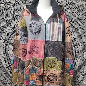 May include: A long-sleeve zip-up hoodie featuring a patchwork design of various fabric squares in shades of gray, red, yellow, and blue. The garment displays printed graphics of suns, mushrooms, and geometric patterns, with visible white cross-stitching.
