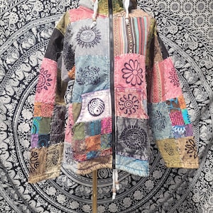 May include: A long-sleeve hooded jacket featuring a patchwork design of various colorful fabrics. The jacket includes a black front zipper, white drawstring cords, and printed graphics of suns, flowers, and mushrooms across the panels.