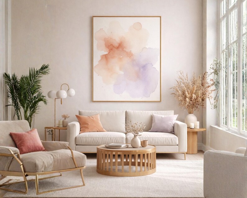 May include: A living room scene featuring a large abstract watercolor painting in a gold frame. A cream-colored sofa with peach and lavender pillows sits below the artwork. A round wooden coffee table and a gold-framed armchair complete the decor.