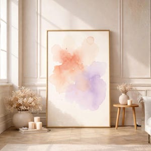 May include: A large framed watercolor art print featuring a soft, abstract design in shades of peach, coral, and lavender. The artwork is displayed in a bright, airy room with a neutral color palette, complemented by a wooden side table and a white sofa.