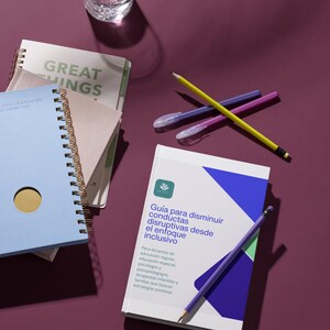 Peut inclure: Une nature morte avec des cahiers, des stylos et un verre d'eau sur une surface violette. Les cahiers sont à spirales, dont un bleu clair et un autre avec le texte "GREAT THINGS". Un livre avec du texte en espagnol est également présent.