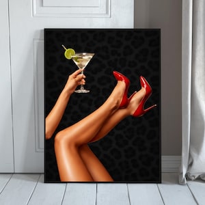 Peut inclure: Impression encadrée représentant des jambes féminines chaussées de talons aiguilles rouges et une main tenant un verre à martini garni de citron vert. Le fond est noir avec un motif léopard. L'image est affichée sur un mur blanc.