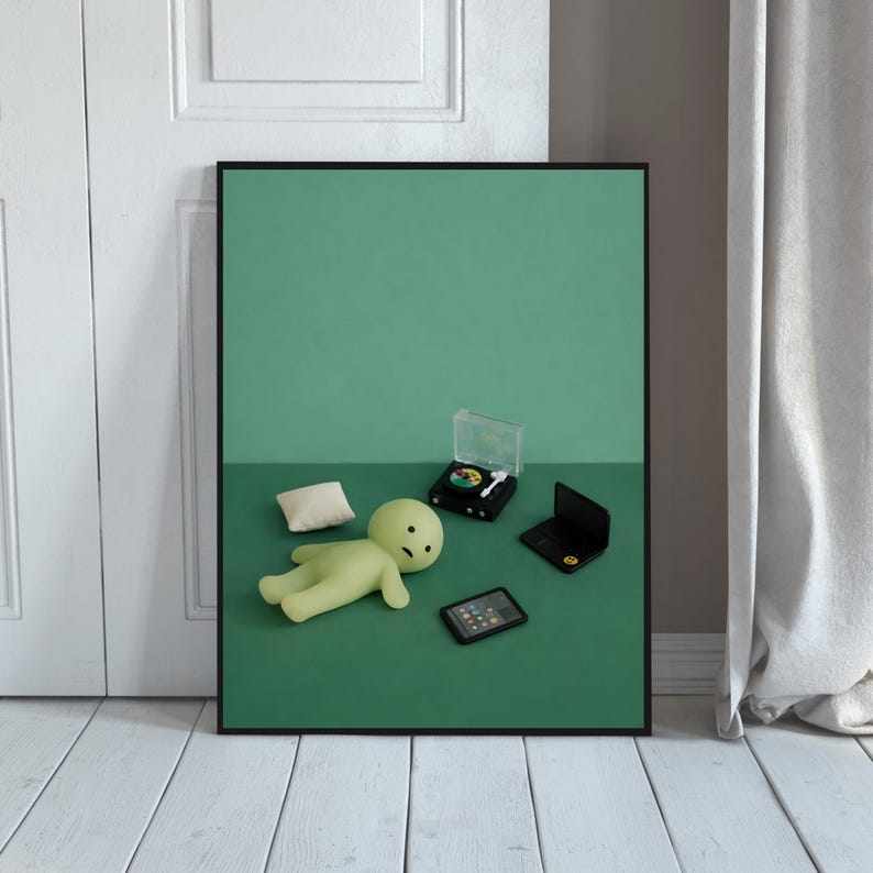 May include: A framed art print featuring a whimsical scene with a green figure, a small pillow, a miniature record player, a laptop, and a tablet, all arranged on a green surface. The artwork has a minimalist aesthetic with a playful, modern vibe.