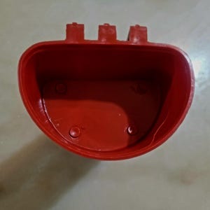 Może przedstawiać: Czerwony plastikowy pojemnik z zaokrąglonym dnem i trzema prostokątnymi wypustkami na górnej krawędzi. Wnętrze jest gładkie, a pojemnik ma trzy małe okrągłe wklęsłości na dnie.