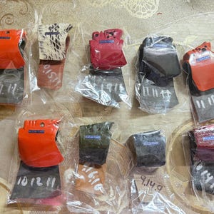 Puede incluir: Una variedad de protectores de cabeza de hacha en envases de pl&aacute;stico transparente. Los protectores son de varios colores, incluyendo naranja, rojo, negro y beige estampado. Cada protector tiene una etiqueta con el texto "PELICAN POWER". Las cabezas de hacha tienen n&uacute;meros escritos a mano.