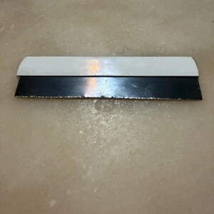 May include: A paint scraper with a white handle and a black blade. The blade shows signs of wear and tear. The tool is designed for removing paint or other materials from surfaces.
