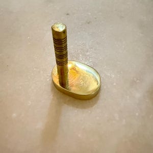 May include: A small, gold-colored object with a rounded base and a vertical, cylindrical post. The post has horizontal grooves. The object is likely a decorative item or a small stand.