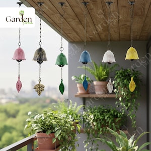 May include: A collection of hanging wind chimes in various colors, including pink, green, blue, white, and yellow. Each chime features a bell-shaped top and a decorative leaf or leaf-shaped pendant. The chimes are suspended from a wooden ceiling.