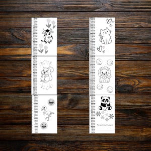 May include: Two white growth charts with black and white illustrations of animals and flowers. The charts measure up to 150 cm. One chart features a cow, squirrel, flamingo, and emojis. The other chart features a cat, lion, panda, and flowers.