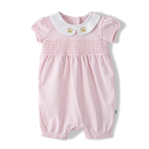 May include: A light pink baby romper with a white collar. The collar has two gold crown designs. The romper has short sleeves and a smocked bodice. The bottom of the romper has elastic around the legs.