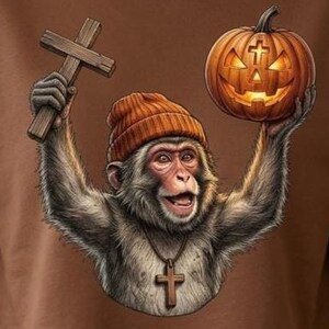May include: A brown long-sleeve crop sweatshirt featuring a graphic of a monkey wearing an orange beanie and a cross necklace. The monkey holds a wooden cross in one hand and a glowing jack-o'-lantern pumpkin with a cross carving in the other.