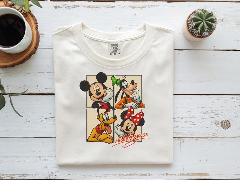 以下が含まれることがあります： クリーム色の半袖Tシャツ。ミッキーマウス、グーフィー、プルート、ミニーマウスが4つのパネルのグリッドに配置されたグラフィックプリントが施されています。前面のキャラクターの下には、赤い筆記体でMickey Mouseの文字がプリントされています。