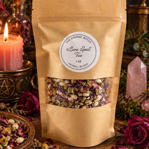 May include: A brown paper pouch containing a herbal blend, featuring a clear window to view the dried flowers and herbs inside. A white circular label on the front reads: The Greene Witch, Love Spell Tea, 1 oz, Herbal Blend.