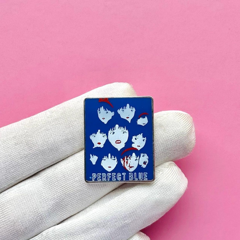 Pode incluir: Um alfinete de esmalte azul com um design do filme de anime "Perfect Blue". O alfinete retangular mostra v&aacute;rios rostos estilizados com detalhes em vermelho. O texto "PERFECT BLUE" est&aacute; na parte inferior.
