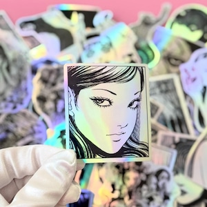 May include: A white ceramic mug with a black handle and the text "But First, Coffee" in a bold, black font. The mug is set against a blurred background, suggesting a cozy setting.