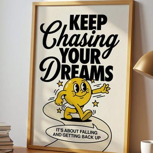 May include: A framed poster with the words "Keep Chasing Your Dreams" and a cartoon character. The poster is on a wooden desk with a lamp, books, and a mug. A potted plant sits near a window.