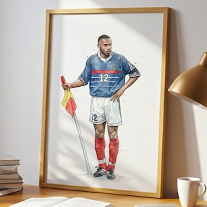 Peut inclure: Une impression encadrée d'aquarelle d'un joueur de football en maillot bleu, numéro 12, tenant un drapeau. L'œuvre est sur un bureau en bois avec une lampe, des livres et une tasse.