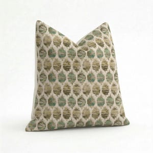 May include: A decorative pillow with a repeating pattern of teal and olive-green circles on a cream background. The pillow has a soft, textured appearance and is designed for home decor.