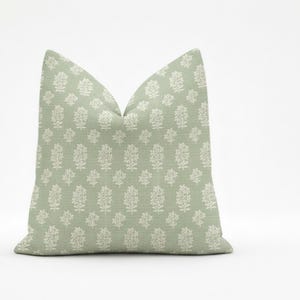 May include: A sage green decorative pillow with a repeating white floral pattern. The pillow is square and has a soft, textured appearance. The design features stylized floral motifs, creating a fresh, botanical theme.