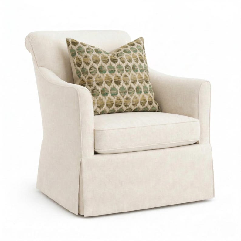 May include: Cream-colored upholstered armchair with a matching skirt and rolled arms. A decorative pillow with a green and tan geometric pattern rests on the seat. The chair is designed for comfort and style.