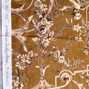May include: Close-up of a fabric with a detailed floral and cherub design in shades of brown and cream. The fabric features roses, daisies, and scrolling vines. Text on the side reads "EGLANTINE" printed in Switzerland, &copy; MCMXCV.