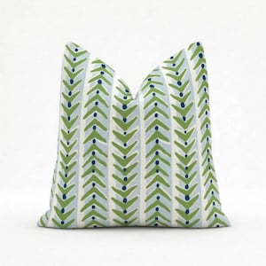 May include: A square decorative pillow with a repeating pattern of green arrow shapes and navy blue dots on a light blue and white striped background. The pillow is a soft, inviting accent for any room.