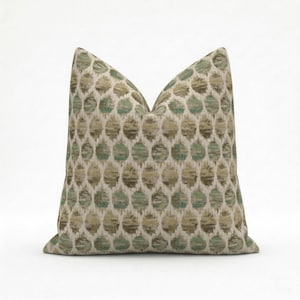 May include: A decorative pillow with a repeating pattern of green and tan circles on a cream background. The pillow has a soft, textured appearance and is designed for home decor.