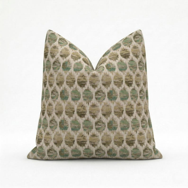 May include: A decorative pillow with a repeating pattern of green and tan circles on a cream background. The pillow has a soft, textured appearance and is designed for home decor.