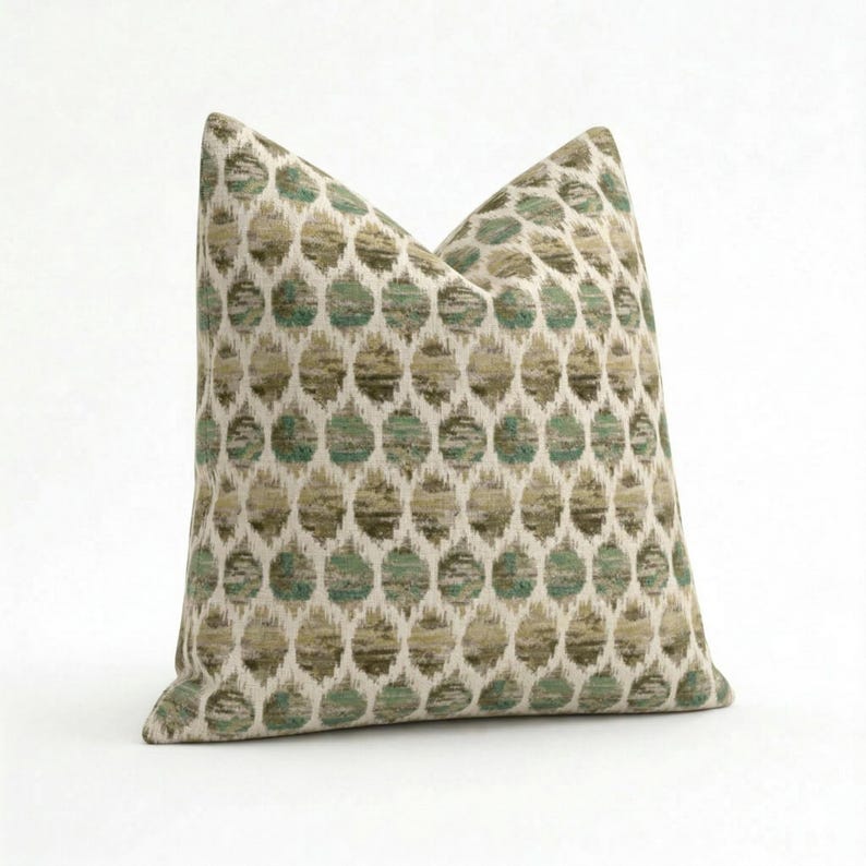 May include: Square decorative pillow with a repeating pattern of green and tan circles on an off-white background. The pillow has a soft, textured appearance and is likely made of fabric.
