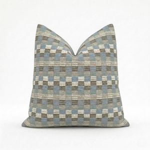 May include: A square cushion with a geometric pattern in shades of blue, grey, and white. The cushion has a textured appearance and a soft look. The pattern consists of a repeating checkerboard design.