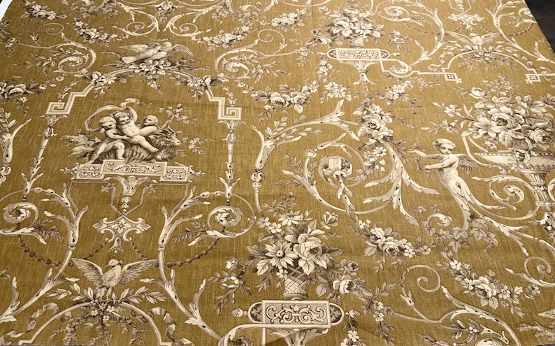 May include: Mustard-colored fabric with a repeating pattern of cherubs, birds, and floral bouquets in shades of white and brown. The fabric has a vintage, classical design, suitable for upholstery or decorative projects.