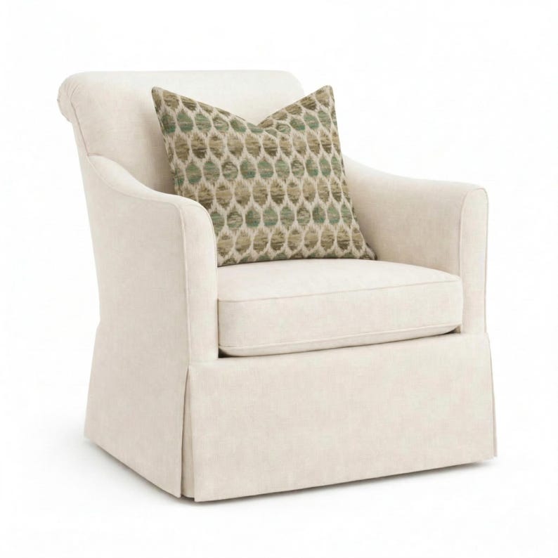 May include: Cream-colored upholstered armchair with a matching skirt. A decorative pillow with a green and tan geometric pattern rests on the seat. The chair has curved arms and a comfortable design, suitable for a living room or bedroom.
