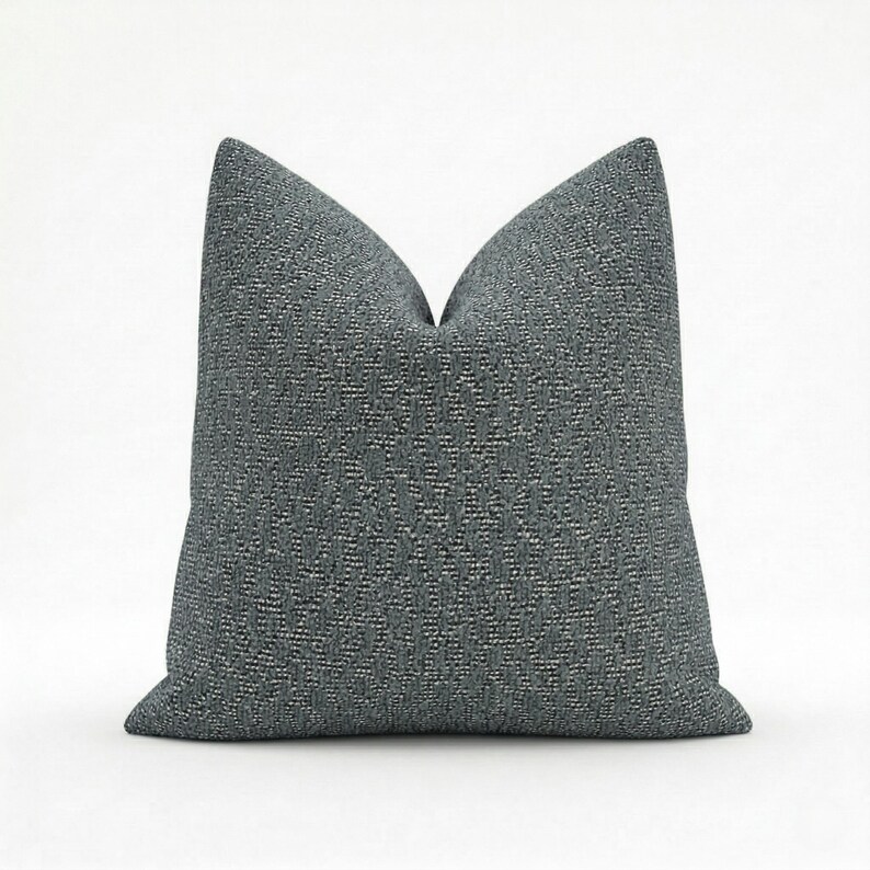 May include: A square, textured throw pillow in a dark gray color. The pillow has a woven pattern and a soft, inviting appearance. The pillow is designed for decorative use on a bed or sofa.