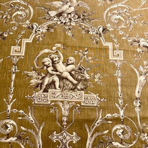 May include: Mustard-colored fabric with a detailed toile pattern. The design features cherubs, floral arrangements, and architectural elements in shades of white and gray. The fabric has a vintage aesthetic.