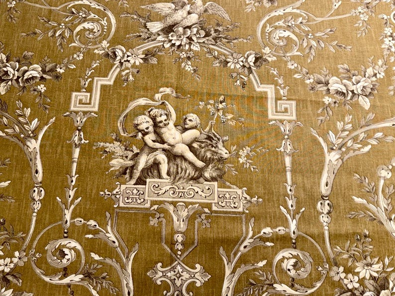 May include: Mustard-colored fabric with a detailed toile pattern. The design features cherubs, floral arrangements, and architectural elements in shades of white and gray. The fabric has a vintage aesthetic.